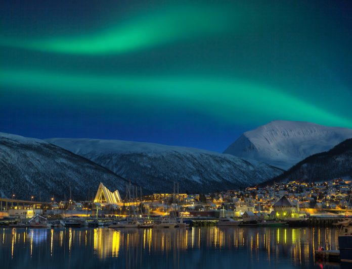 View at night on illuminated Tromso city with cathedral and majestic aurora borealis noche polar