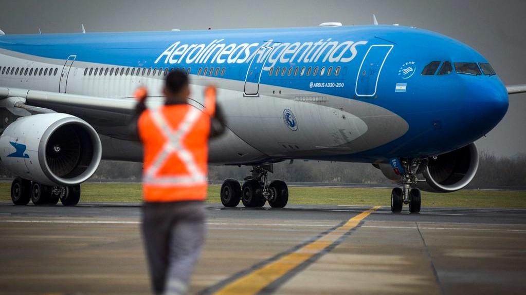 Avión de Aerolíneas Argentinas aterrizando en un aeropuerto mientras un asistente de tráfico lo guía