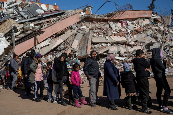 Foto de archivo de un grupo de personas haciendo fila para recibir alimentos frente a un edificio destruido en la localidad turca de Kahramanmaras terremoto en siria
